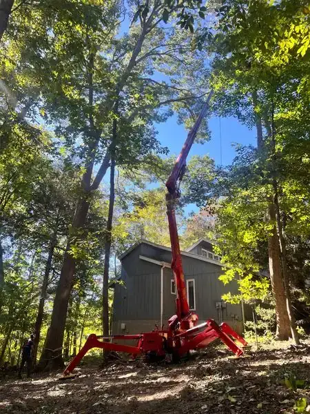 Red spider lift deployed in a wooded lot beside a grey house under a fall canopy